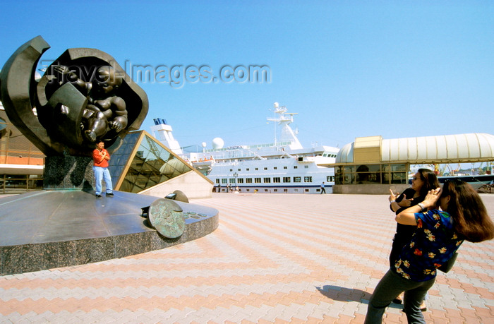 ukra35: Odessa, Ukraine: woman taking picture of man standing at a statue of a hatching baby, called the 'Golden boy' by sculptor Ernst Neizvestny - Maritime Terminal area - cruise ship Arkona in the dock - photo by K.Gapys - (c) Travel-Images.com - Stock Photography agency - Image Bank