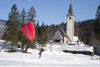 Slovenia - Ribcev Laz - man preparing to paraglide across a frozen Bohinj Lake - St John's church in the background - photo by I.Middleton
