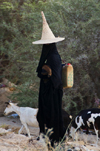 Wadi Hadhramaut, Hadhramaut Governorate, Yemen: local woman tending goats - she carries a baby goat and a jerry-can and wears an abaya and a madhalla conical hat, made of dried palm leaves - photo by J.Pemberton